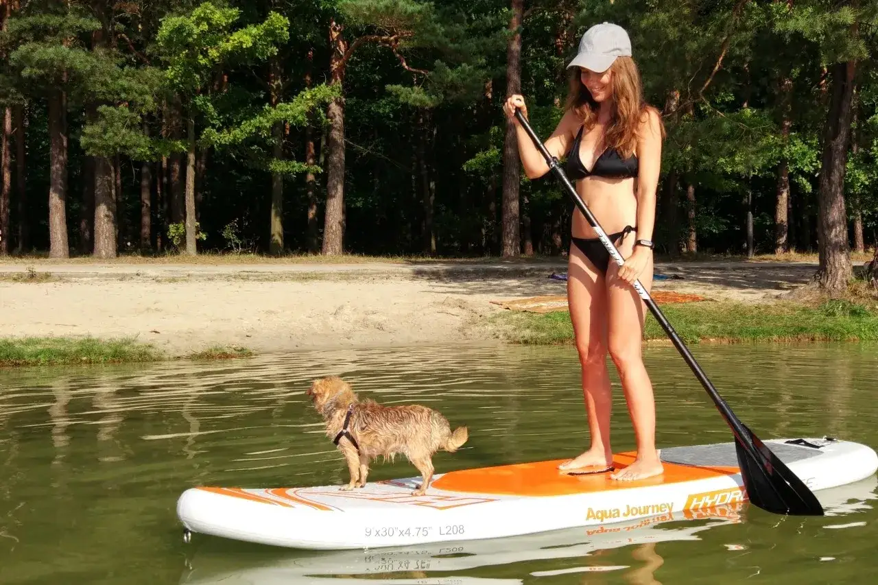 Dziewczyna na desce SUP z psem, relaksują się na jeziorze. Co to jest SUP? To sport wodny, który pozwala cieszyć się naturą.