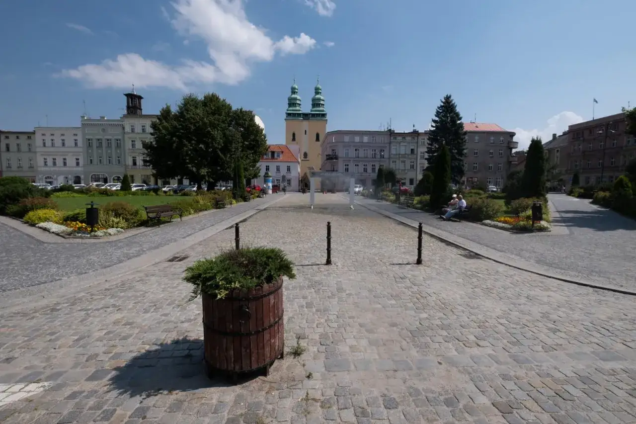 Rynek w Głuchołazach z zabytkową architekturą i zielenią. Atrakcje miasta, takie jak fontanna, zachęcają do odpoczynku.