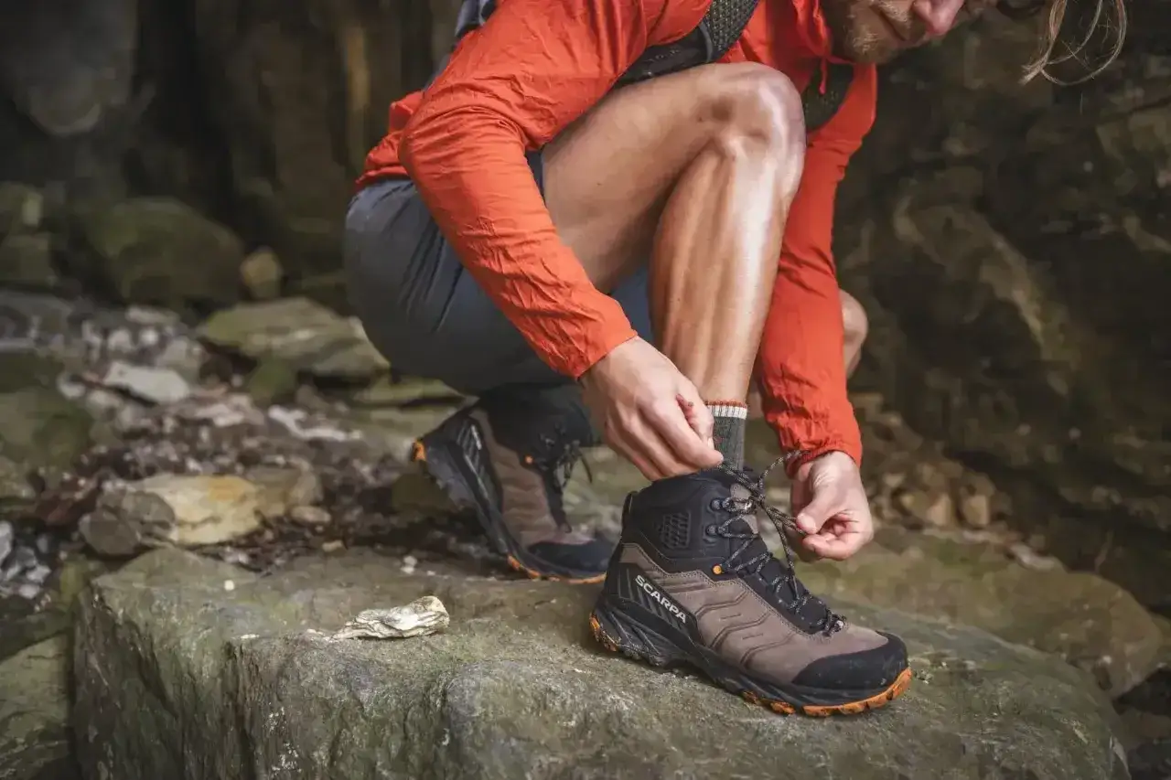Wybierasz jakie buty w Bieszczady? Ten turysta wiąże swoje solidne, brązowo-czarne buty trekkingowe Scarpa na kamienistym szlaku.