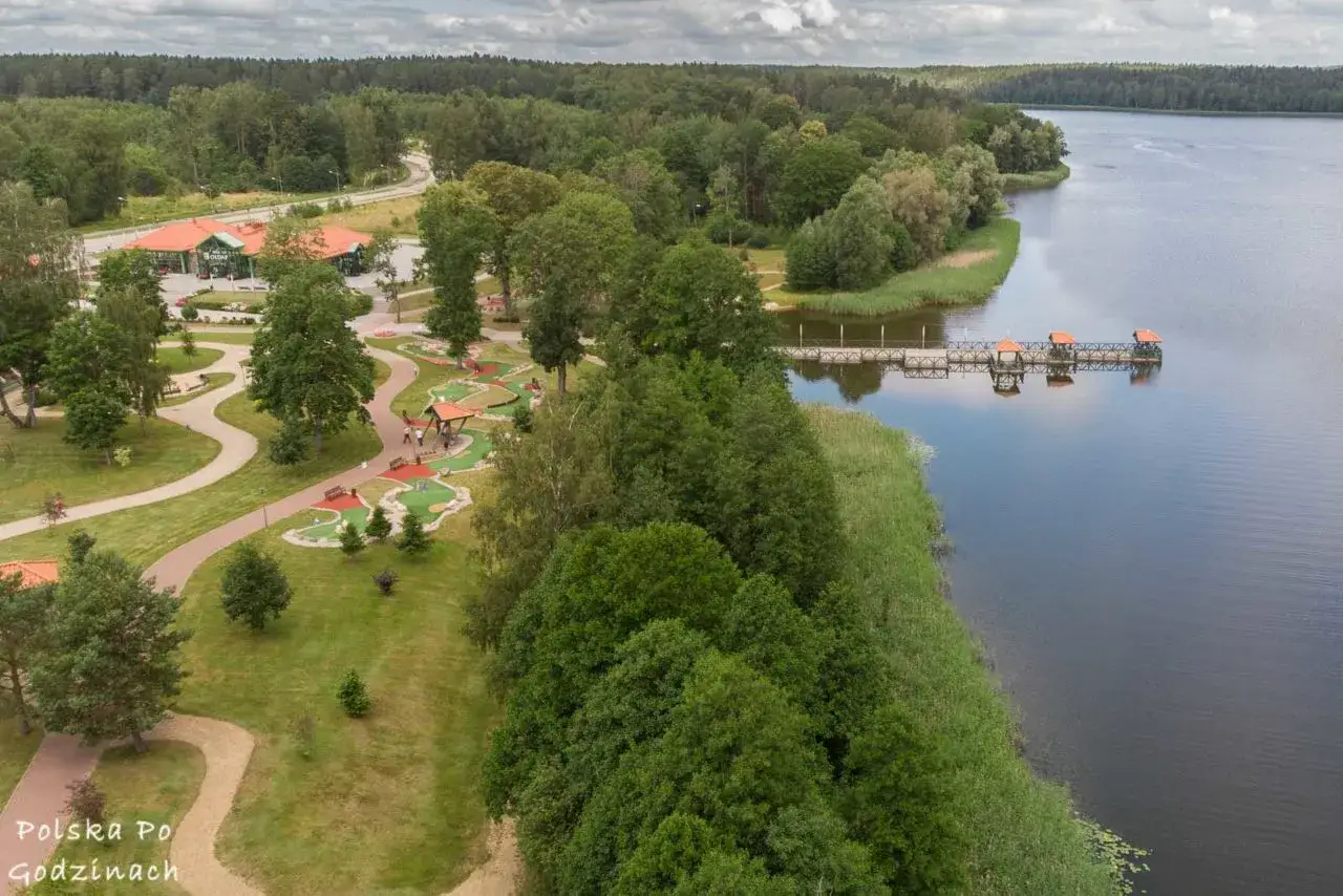 Gołdap atrakcje: malowniczy widok na jezioro z pomostem i polem do minigolfa, otoczone zielenią.
