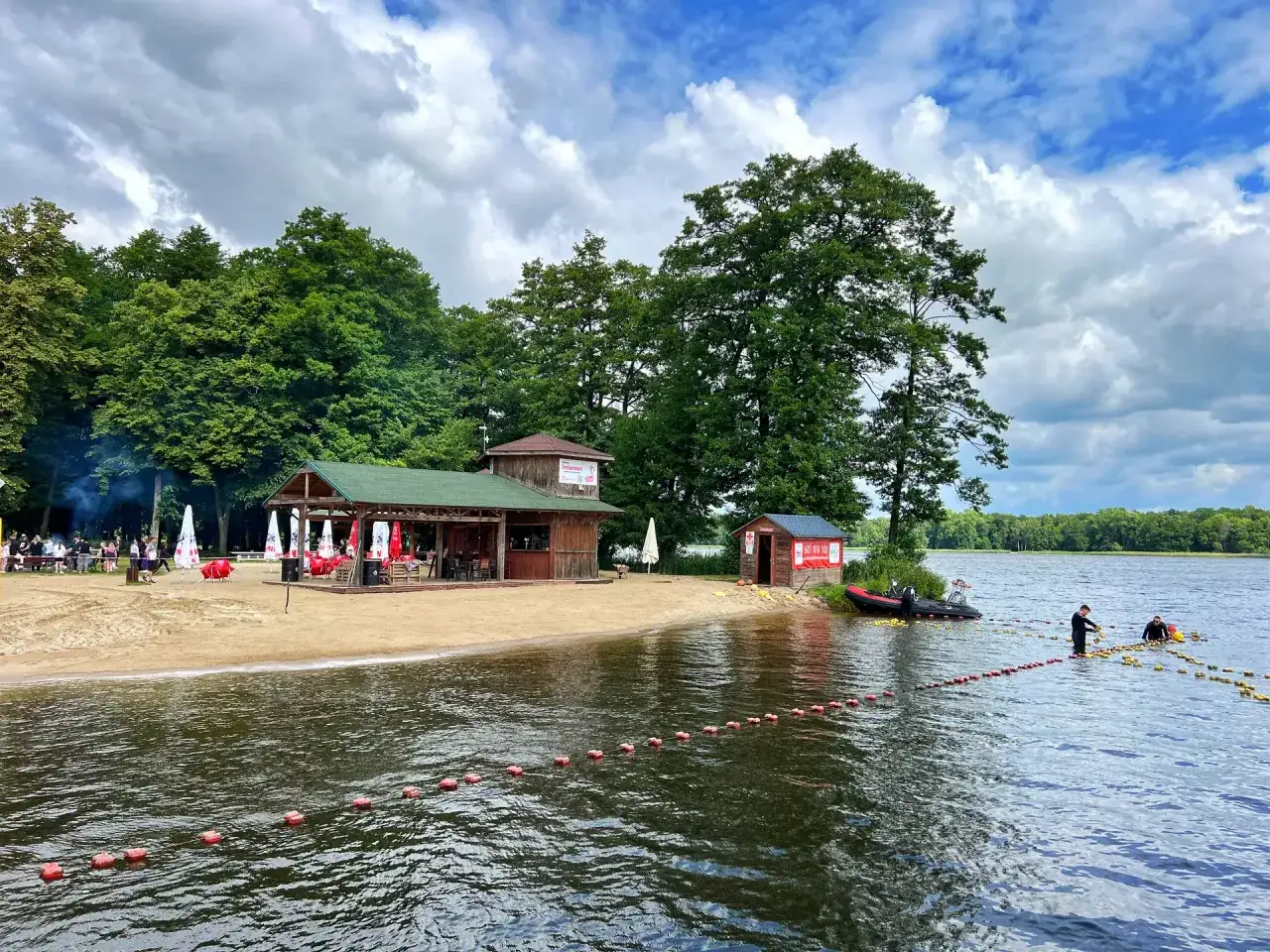 Plaża i jezioro w Szczecinku. Drewniane budynki, łódź i ratownicy na wodzie. Idealne miejsce na letnie atrakcje.