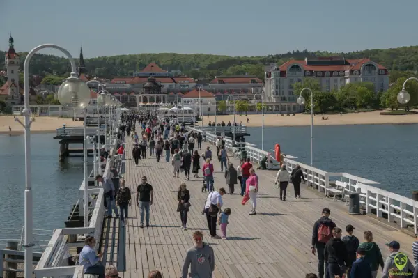 Tłum ludzi spaceruje po molo w Sopocie, jednym z najpopularniejszych gdańsk atrakcje. W tle widać plażę i zabytkowe budynki.